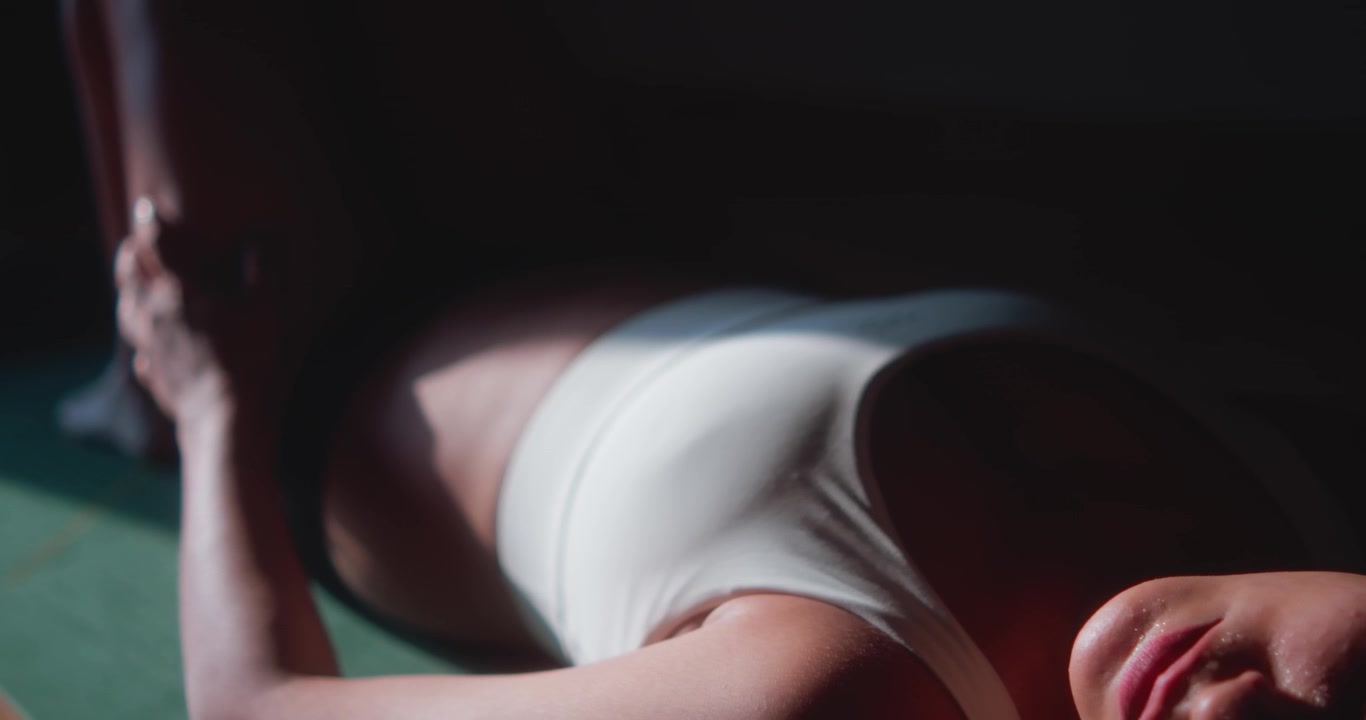Frau in Sportkleidung dehnt sich auf einer Yogamatte in Innenräumen, Sonnenlicht fällt auf ihren Körper.