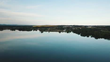 shot of a drone on a clear water surface. calm lake without waves and reflecting water. water tank from a bird's eye view. a biotope that is filmed after the golden hour. czechia, south moravia