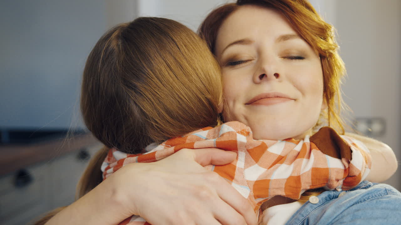 Portrait shot of the attractive young caucasian woman hugging a little girl who coming to her tight. Rear of the girl. Close up. Indoors