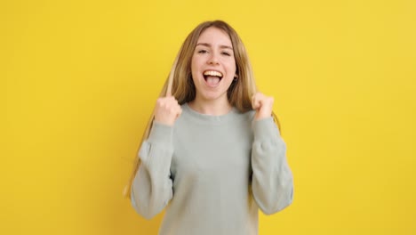 young woman celebrating success on bright yellow background