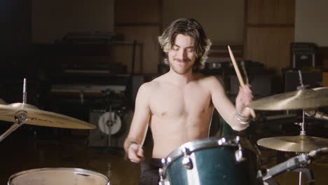 young shirtless male drummer with beard playing drums