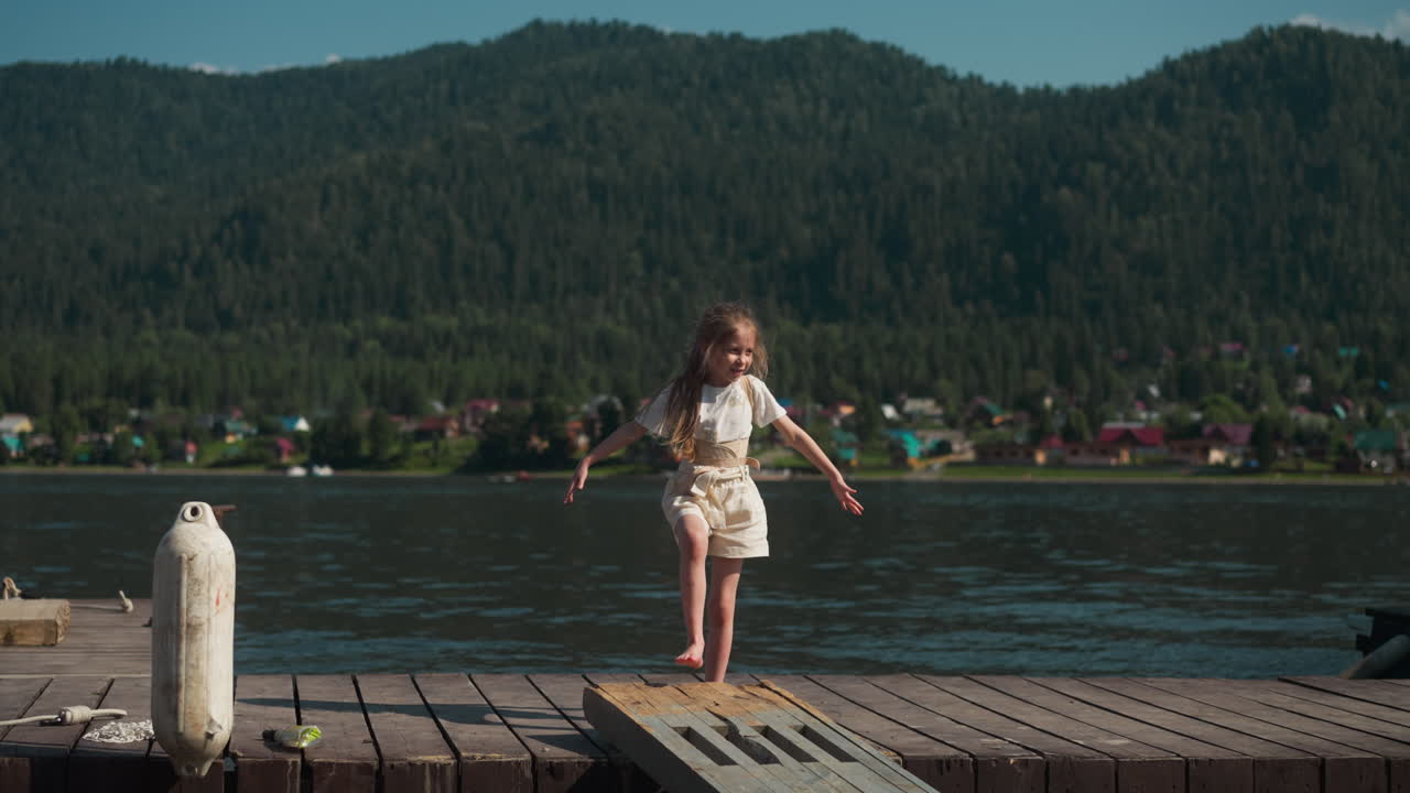chica alegre agita los brazos a los lados moviéndose a lo largo del puente contra las pintorescas montañas. vacaciones en un lugar emocionante para los turistas. vacaciones para familias con niños