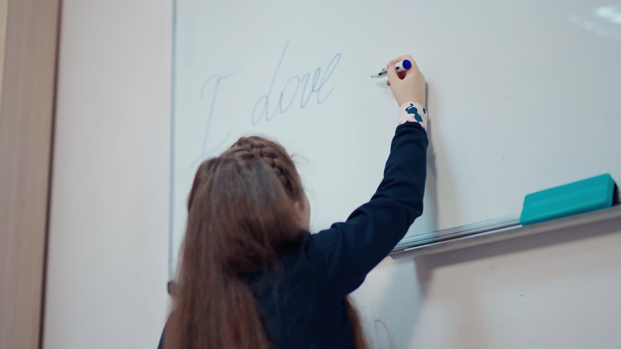 Little girl writing on a whiteboard. Backside view of a schoolgirl in the classroom. Learning process at school. Girl studying in the primary school.
