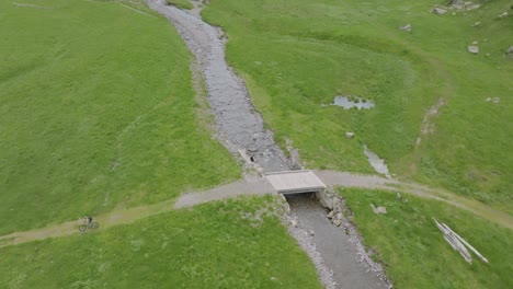 Aerial-top-down-shot-of-mountain-biker-crossing-bridge-in-scenic-area-of-dolomites-mountains-during-summer