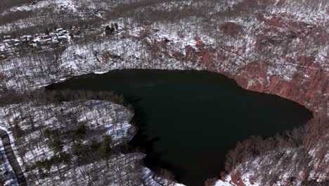 an aerial view of a large emerald colored lake, surrounded by mountains during winter on a sunny day