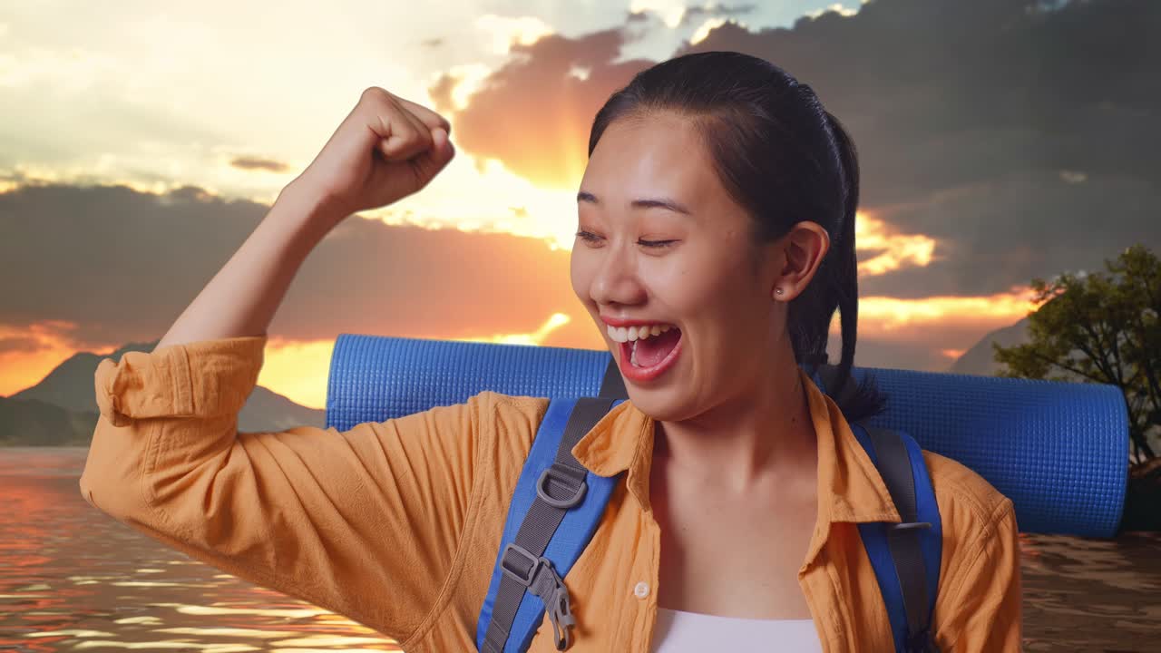 Close Up Of Asian Female Hiker With Mountaineering Backpack Smiling And Flexing Her Bicep While Standing At A Lake During Sunset Time