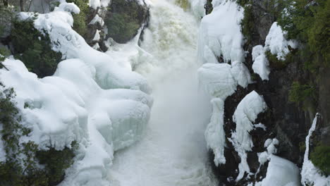 incredible slow motion shot of a river flowing into a frozen waterfall in a forest landscape