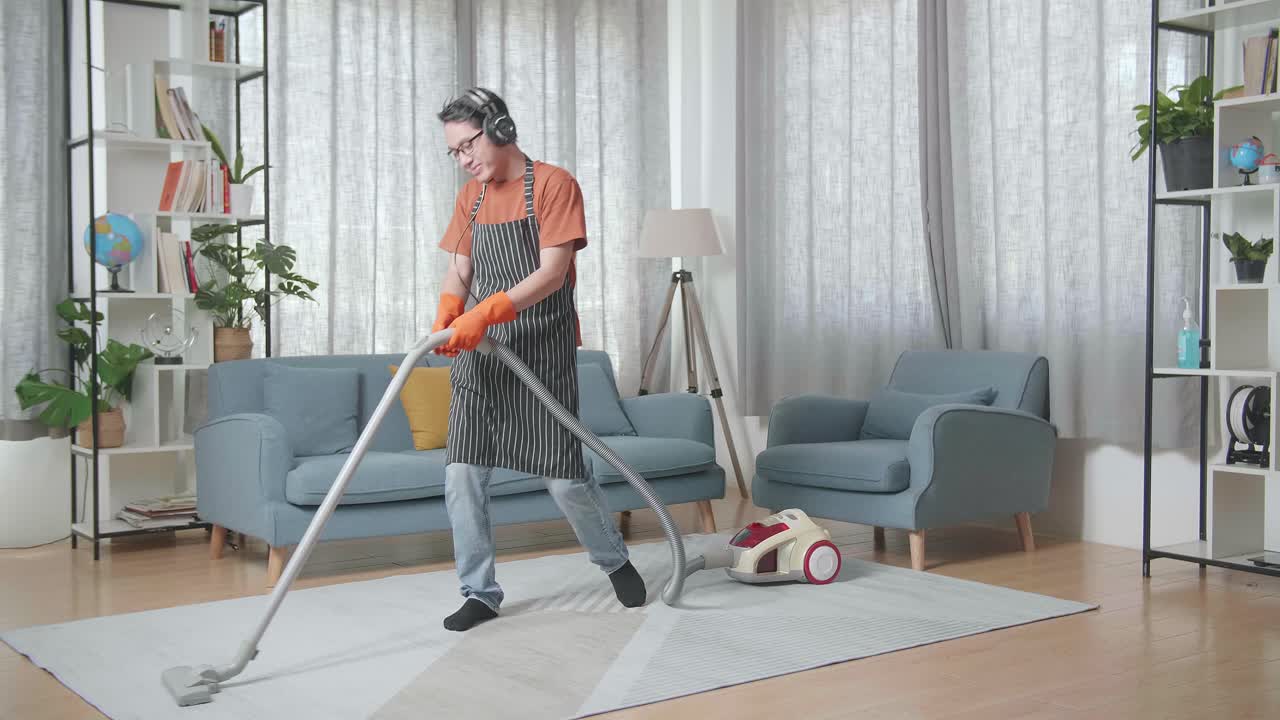 헤드폰 을 착용 하고, 음악 을 듣고, 집 에서 바닥 을 청소 하는 동안 춤 을 추는 아시안 남자 집주인