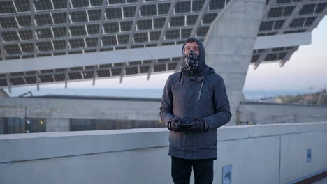 anonymer mann mit kapuze, der die drohne kontrolliert, die im port forum barcelona in der nähe von sonnenkollektoren abhebt