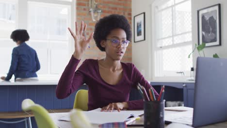 happy african american teenage girl at kitchen table in online lesson using laptop computer