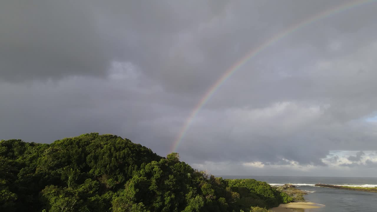 elevándose sobre un promontorio costero verde y exuberante junto a la desembocadura del río aislada con un gran arco iris colorido sobre el océano
