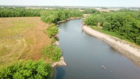 Vista-Aérea-De-Drones-Siguiendo-El-Sendero-De-Agua-Del-Río-Iowa-Y-Varios-Troncos-En-El-Río