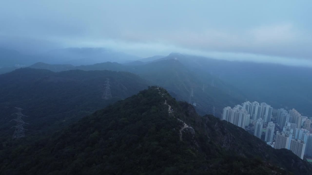 Aerial drone footage gliding over a mountain near Hong Kong Called Lion rock during a cloudy evening day. The area is surrounded by mountains and the air is polluted with smog or it is misty or foggy.