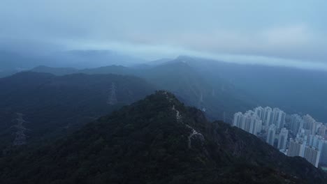 aerial drone footage gliding over a mountain near hong kong called lion rock during a cloudy evening day. the area is surrounded by mountains and the air is polluted with smog or it is misty or foggy.
