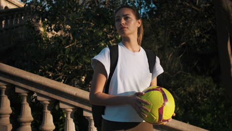 soccer woman with backpack playing with a ball in hands.