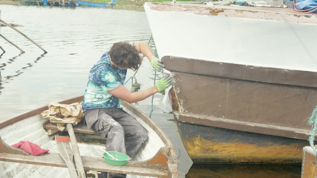 Seorang tukang kayu memasang alas fiberglass pada haluan perahu kayu.