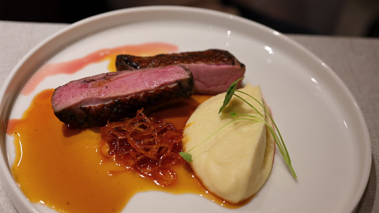 Fine dining duck breast slices served with creamy puree and rich sauce on elegant plate