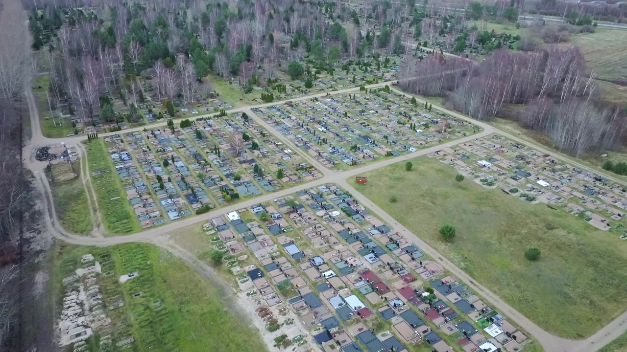Tilt-up cinematografico che rivela il Cimitero Meridionale delimitato da un tranquillo bosco lettone
