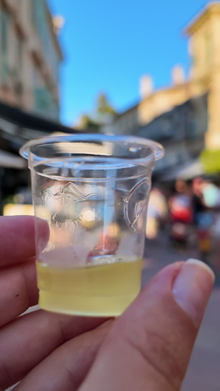 Close up of a woman's hand holding a shot of limoncello on the streets of Menton, France. Vertical