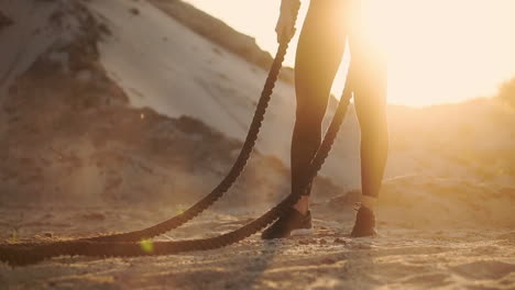 mujer deportiva entrenando alrededor de las colinas de arena al atardecer golpea la cuerda en el suelo y levantó el polvo.