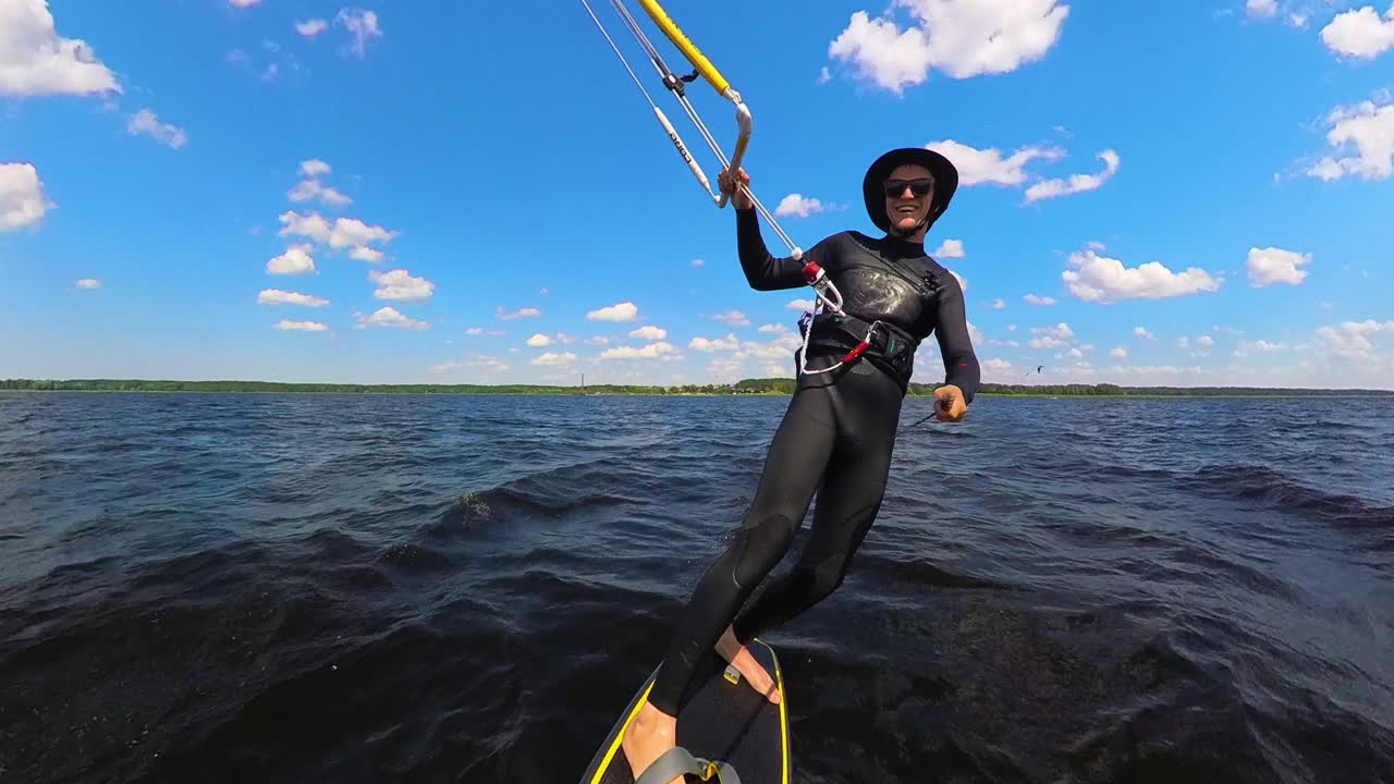 A Man Glides Across the Water on a Kiteboard, Harnessing the Wind Under a Vivid Blue Sky - Tracking Shot