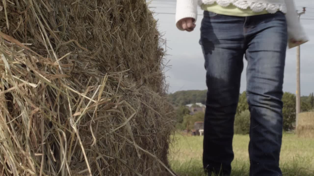 건초 더미 중간 샷을 들고 들판을 걷고 있는 여자