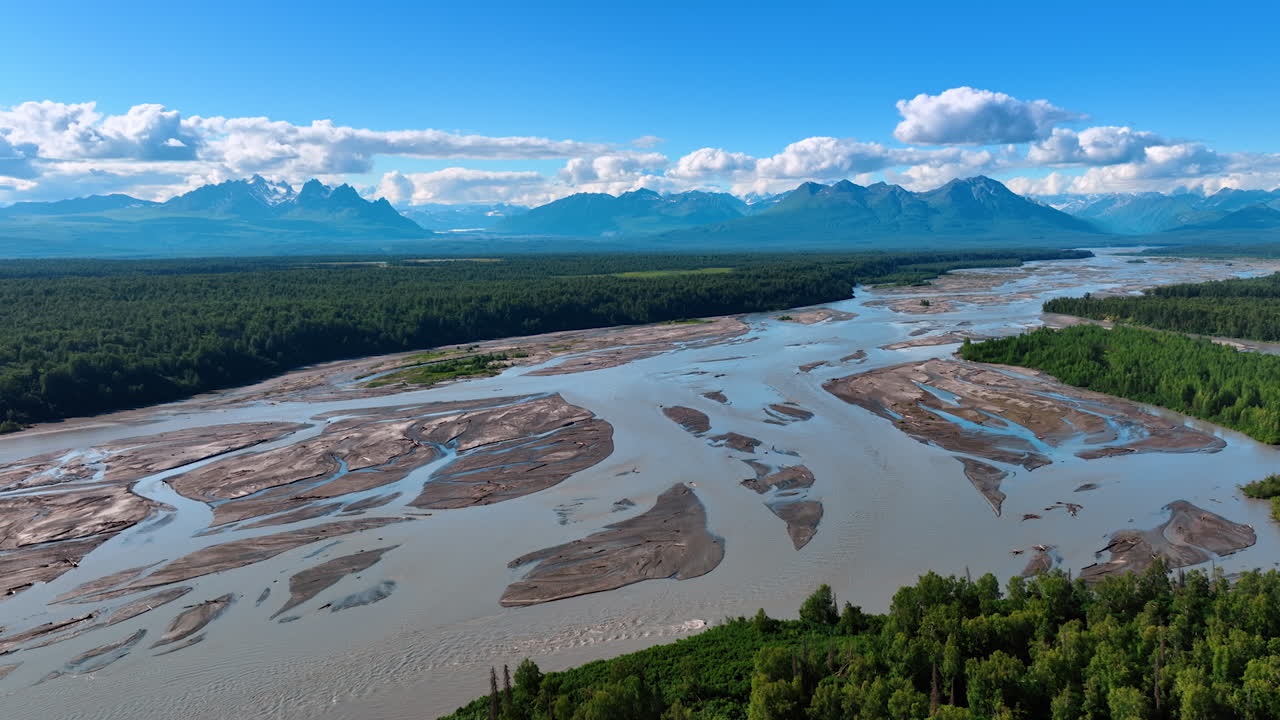 Beautiful river delta in the vast wooded valley. Cumulus fluffy clouds are in the sky over the stunning mountain range. Aerial view. Alaska, US