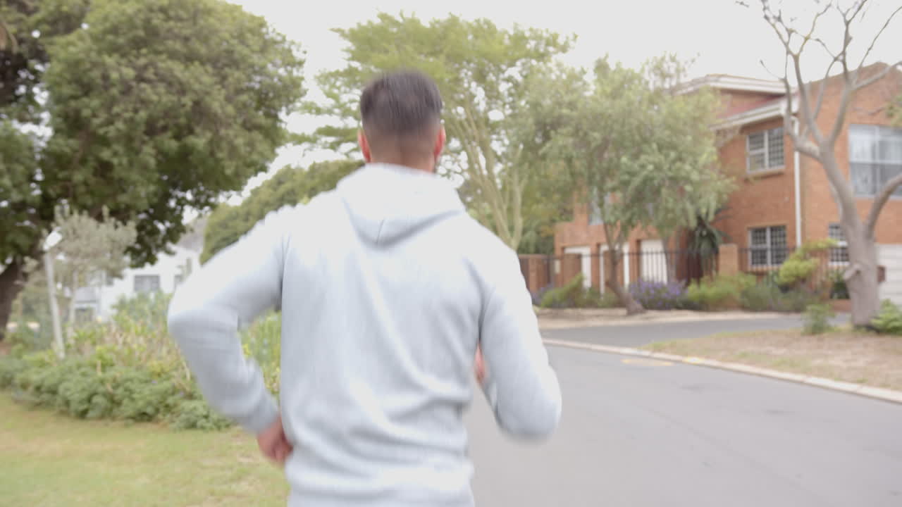 Exercising outdoors, man in hoodie jogging in suburban neighborhood