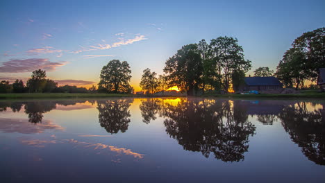 timelapse shot of sunset over colorful sky in the background over lake in front of a wooden cottage at dusk