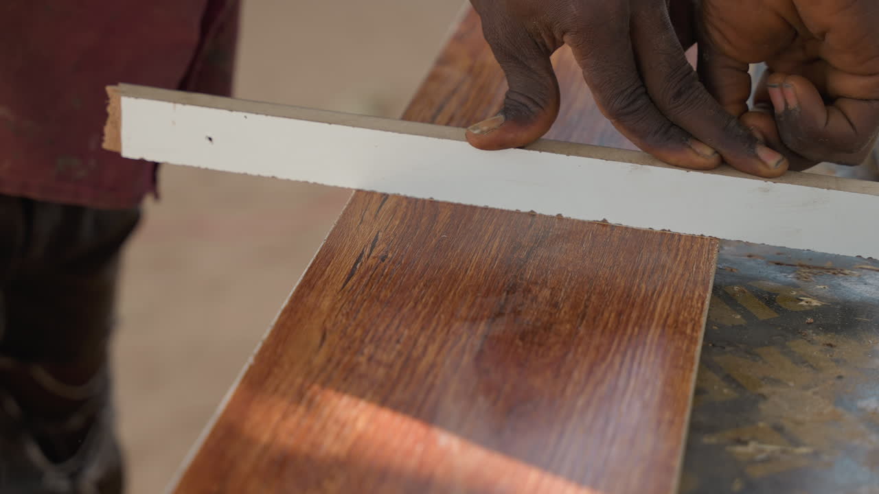 Mani che misurano una tavola di legno su un banco da lavoro. Un professionista della falegnameria segna una linea con righello e gesso, mani guantate e superficie liscia verniciata, misurazione concentrata e preparazione per la falegnameria in officina.