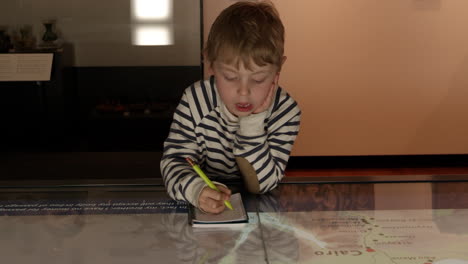 niño en el museo estudia el mapa y escribe en el cuaderno filmado en r3d