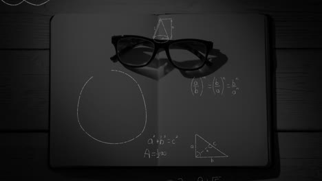 mathematical equations and figures and eyeglass in an open notebook