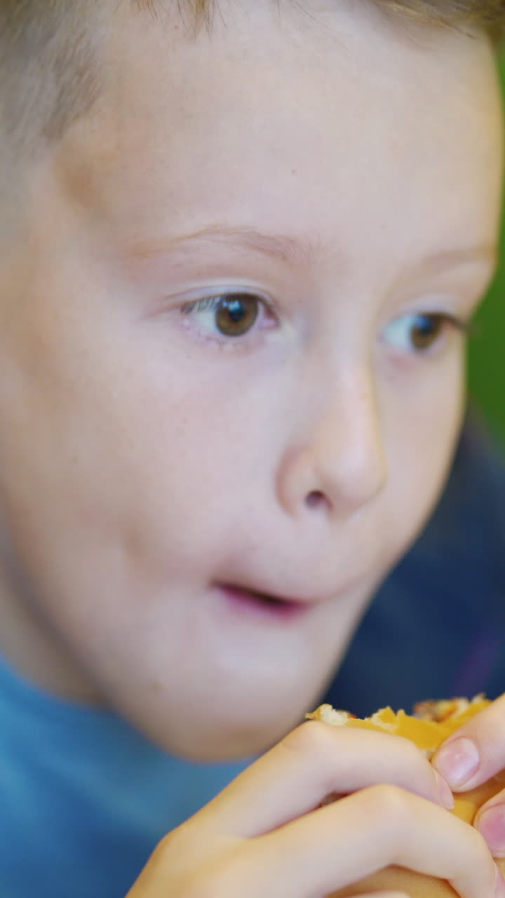 Young teenager eating tasty hamburger in fast food restaurant. Harmful nutrition Vertical video