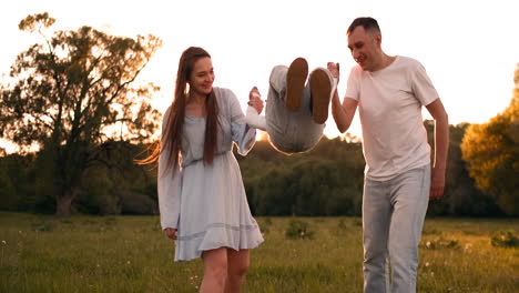 Mama-Und-Papa-Schütteln-Das-Kind,-Das-Auf-Seinen-Händen-Spielt.-Der-Junge-Spielt-Glücklich-Mit-Seinen-Eltern-Im-Sommer-Bei-Sonnenuntergang-Auf-Der-Straße.