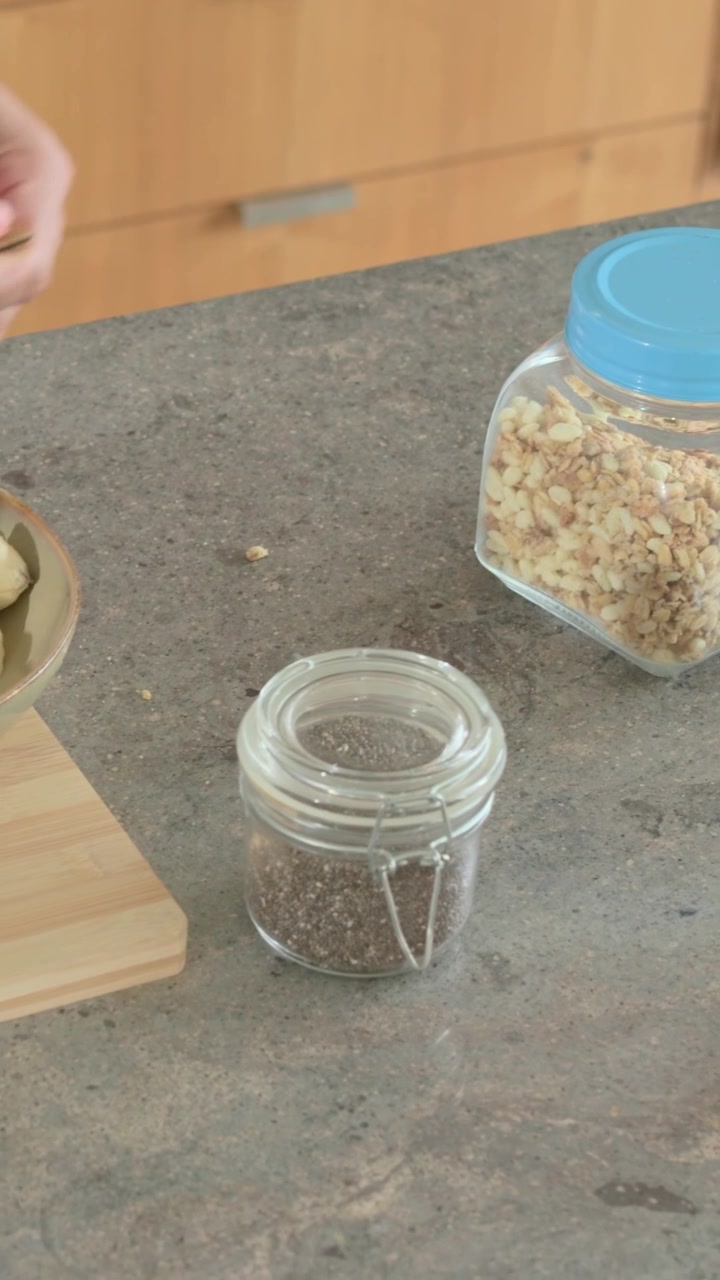 Video verticale: Mano femminile che si allunga spalmando crema sulle banane sul bancone per colazione con semi di chia.
