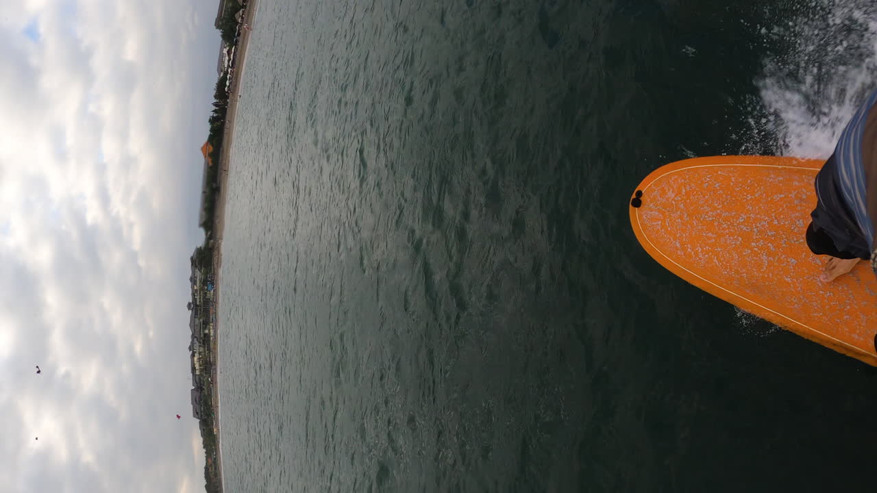 joven surfeando en tablero naranja, video vertical pov