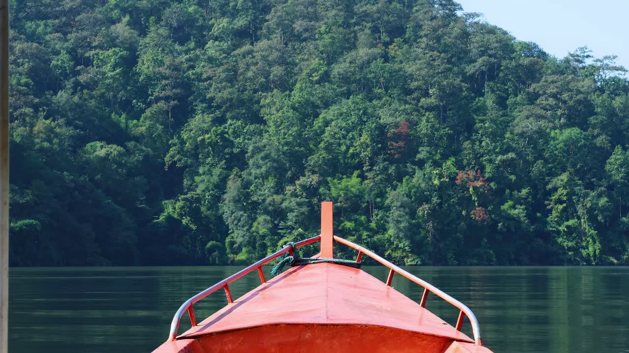 A red boat glides through calm waters surrounded by dense, vibrant greenery.