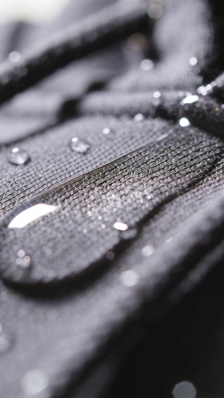 Vertical video: Water drop stretching right on dark seam with light shifting beads staying coating