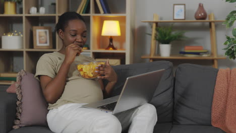 pregnant woman eating chips while working from home
