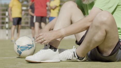 jugador de fútbol senior deportivo sentado en el campo y zapatillas de cordones