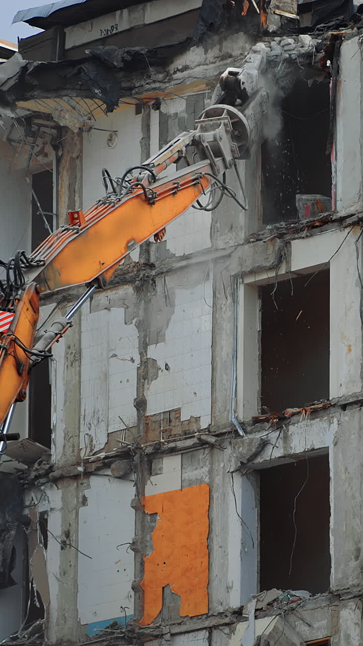 Dismantling the destroyed roof of a high building. Excavator grabber reaches high to demolish the house. Vertical video