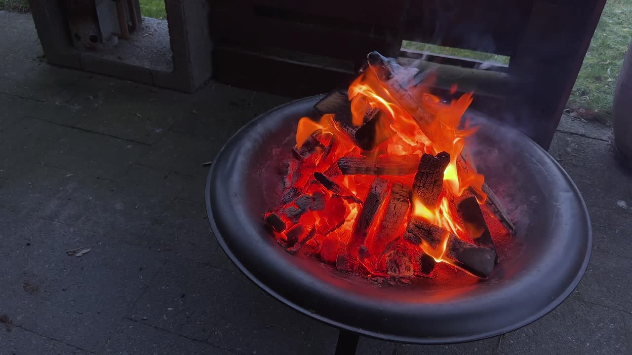 Brasero encendido con llamas naranjas en un patio trasero acogedor. Toma de smartphone. 60 FPS