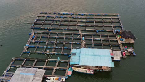 drone low flyover and around a traditional floating fish farms on calm waters, the wooden structures with cages and nets are used for aquaculture