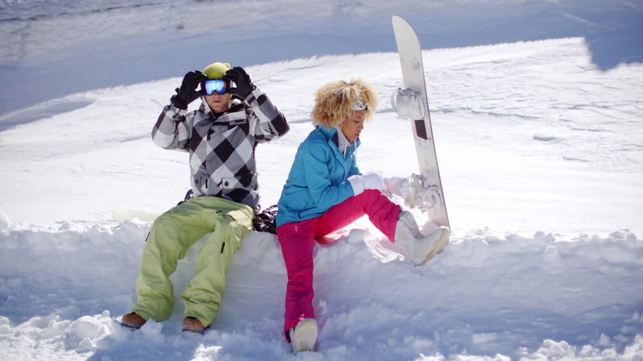 una pareja joven preparándose para ir a hacer snowboard.