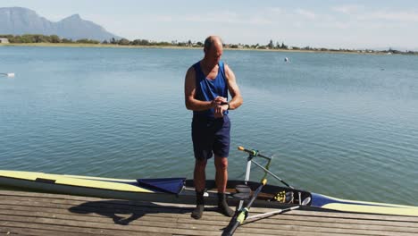 senior caucasian man standing by a river checking smartwatch