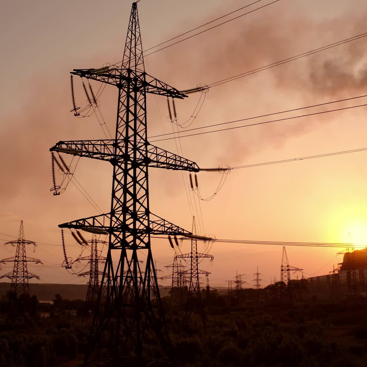 Power station at dusk. Transmission lines near smoke pipes from industrial plant. Chemical emissions in the air from industry. Electric towers with wires at sunset