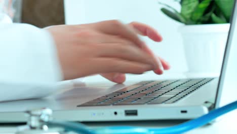 the concept of medicine, the doctor works, the hands of a man in a white robe print the text on the laptop, on the white table a fanendoscope and a dormant green plant