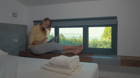 Woman-using-pad-by-the-window-in-hotel