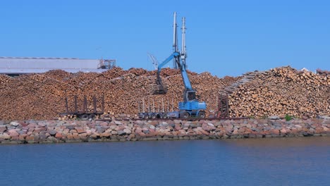 blue forest cargo truck working at dry cargo terminal at port of liepaja in sunny day with clear sky, wide shot over the port channel