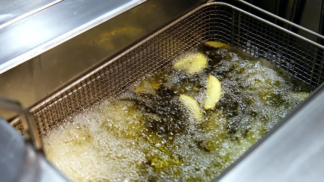 Cooking in deep fryer. Golden potato frying in a hot boiling oil in the restaurant. Crispy vegetables in deep fryer. Unhealthy food.